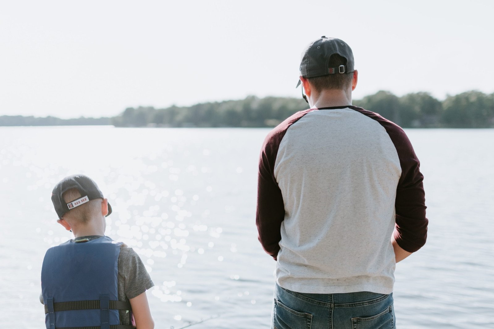 Um homem à direita e um menino pequeno à esquerda, os dois de costas e um pouco afastados em frente ao oceano.