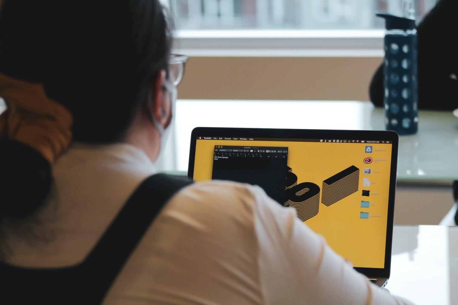 Foto de mulher de costas, câmera sobre o ombro mostrando a tela do seu notebook, que está em uma página amarela e com opções de personalização